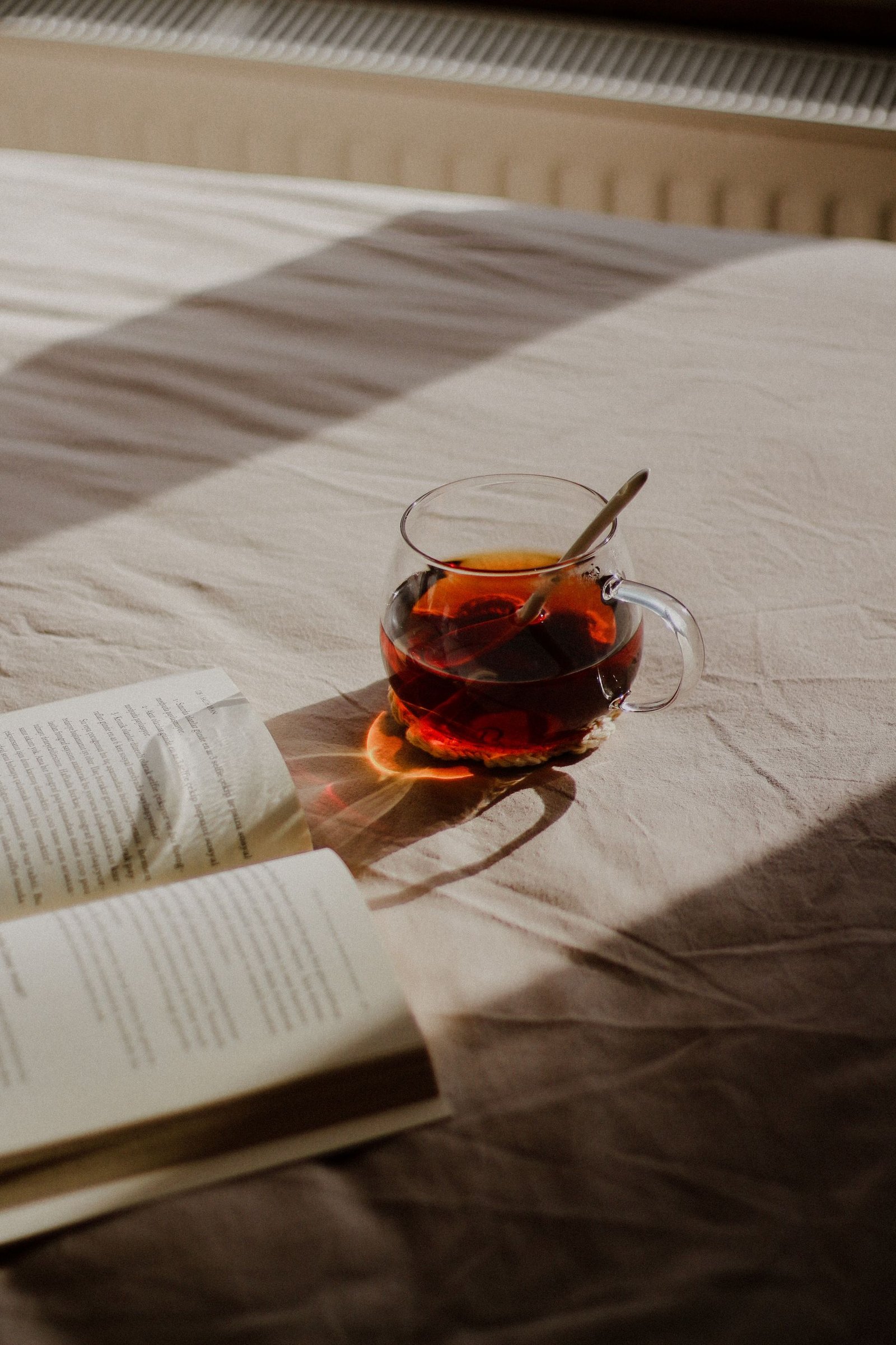 陽だまりのベッドに、読みかけの本と紅茶が置かれた休日の風景。
