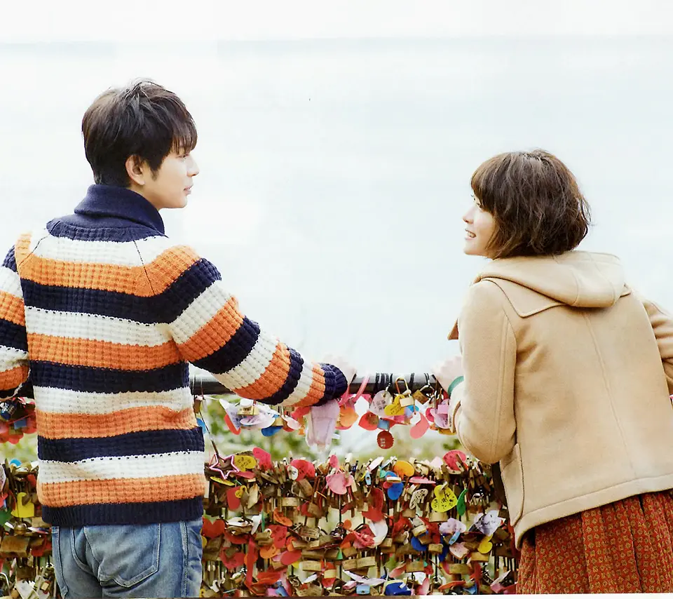 海を背景に南京錠の前で向き合うふたり